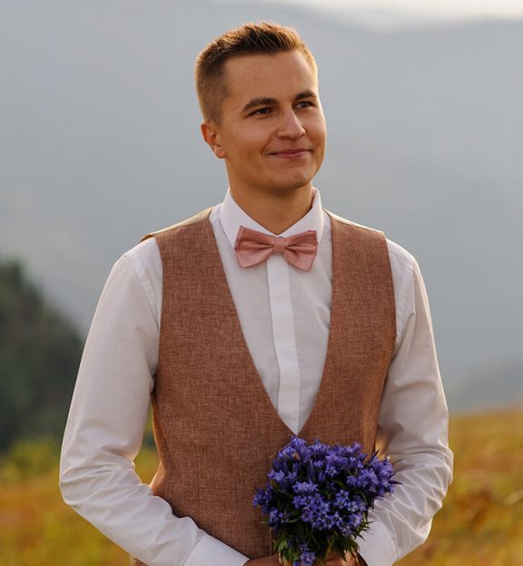 a-groom-with-a-bouquet-of-wildflowers-looks-at-his-2021-09-01-15-25-57-utc