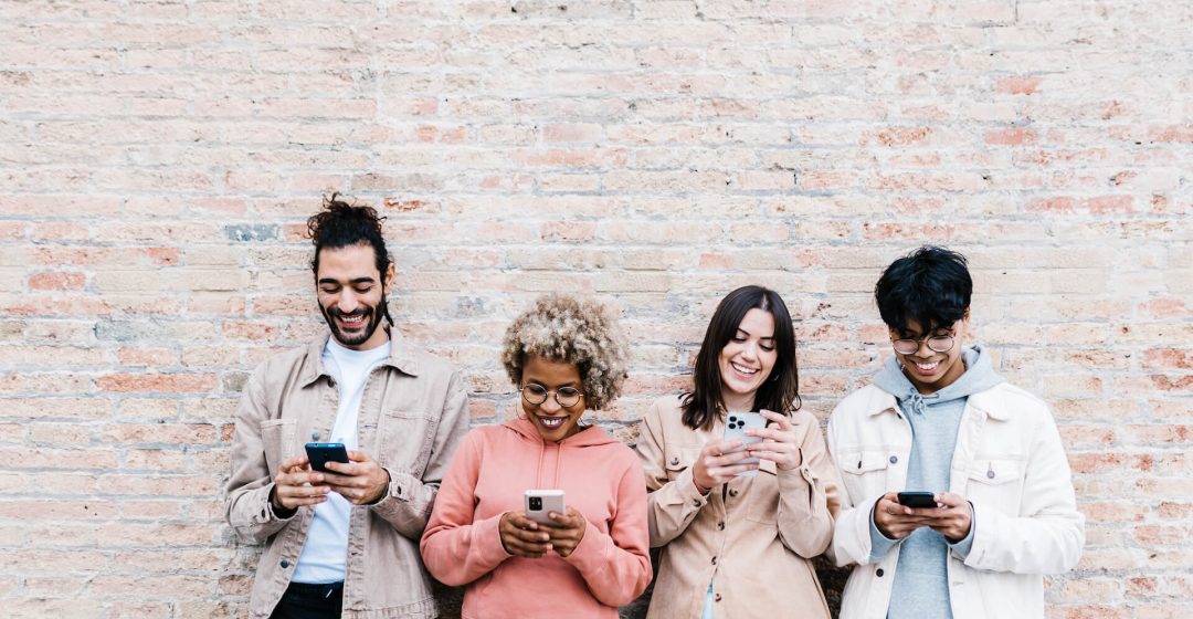 four-multiracial-people-using-mobile-phone-outdoor-2022-03-18-21-00-25-utc