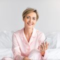 happy-woman-sitting-in-bed-using-cell-phone-2022-01-19-00-11-50-utc